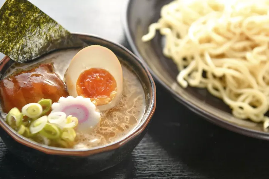 Close-up de uma tigela de macarrão e uma tigela de sopa de ramen com um ovo escalfado, cortado ao meio.